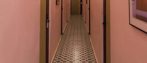 Un corridoio d'albergo con pareti rosa, porte numerate e piastrelle a motivi decorativi.
