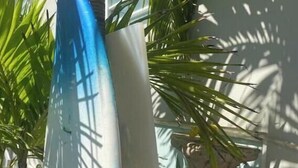 Eine Hausecke mit einer weißen Wand und einem blauen Objekt, möglicherweise einer Skulptur, teilweise verdeckt von Palmenblättern.