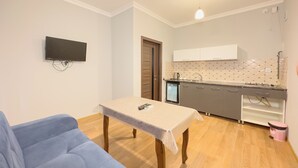 A compact living space with a kitchenette, a sofa, a table with a remote control, and a television mounted on the wall. - River Garden Hotel Gabala (Gabala)