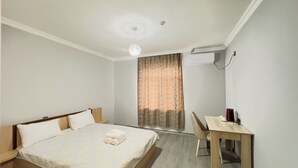 A bedroom with a bed, a desk, and a chair. There is a window with curtains, an air conditioning unit, and a ceiling light. - River Garden Hotel Gabala (Gabala)