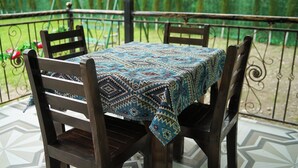 A table with a patterned tablecloth, surrounded by wooden chairs, on a patio with a metal railing and greenery in the background. - River Garden Hotel Gabala (Gabala)