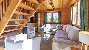 A wooden cabin interior with a staircase, a sofa, and a glass coffee table.
