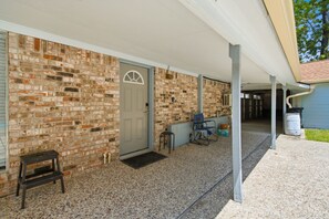 A covered porch with a brick wall, a door, a small table, and a chair.