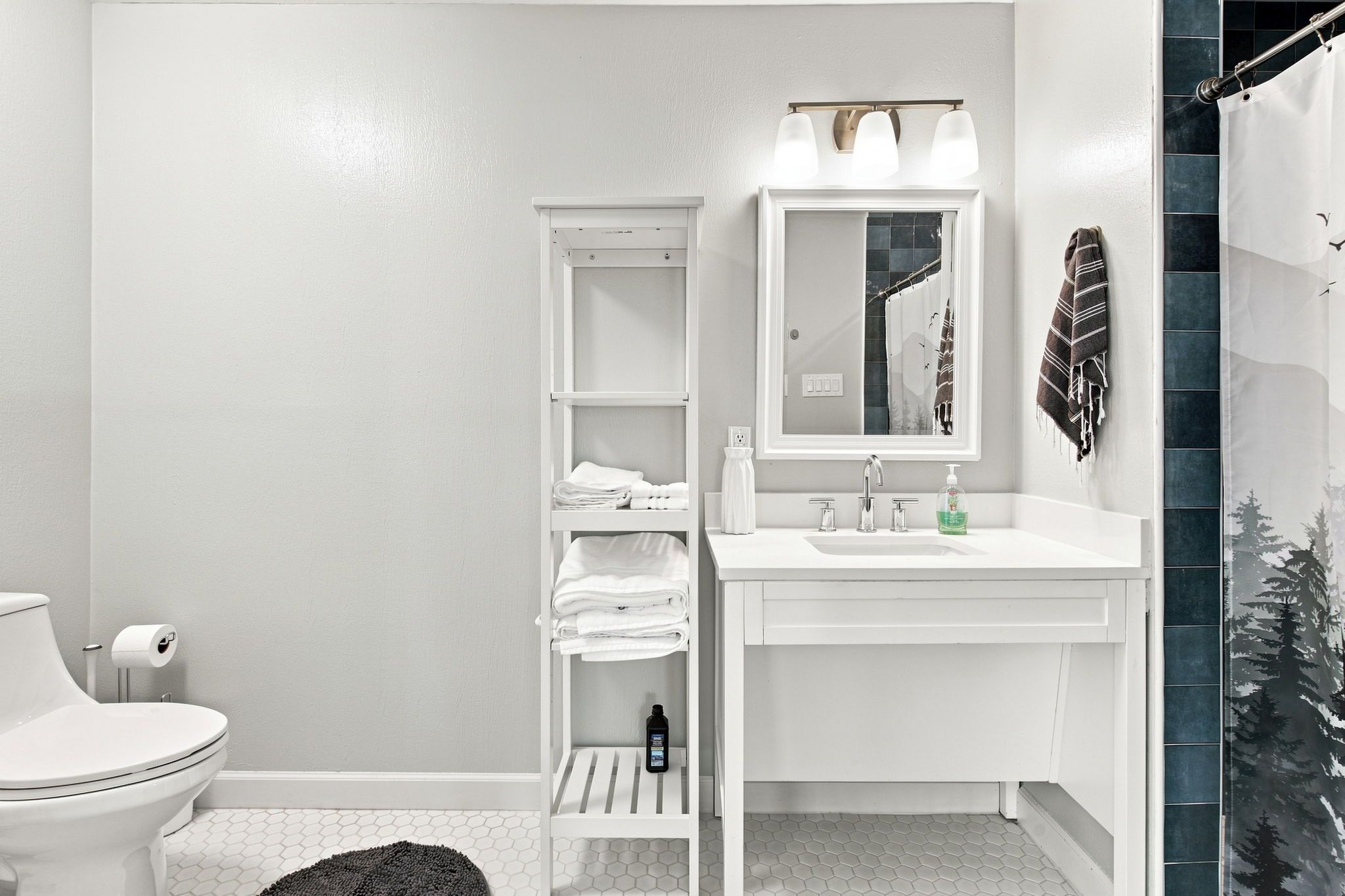 Un baño con inodoro, lavamanos con espejo y un perchero para toallas.
