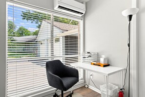 A room with a white desk, a black chair, and a window with blinds.