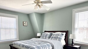 A bedroom with a bed, nightstands, a ceiling fan, and a window with blinds.