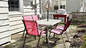A patio with a table and chairs, a hanging umbrella, and a white fence.