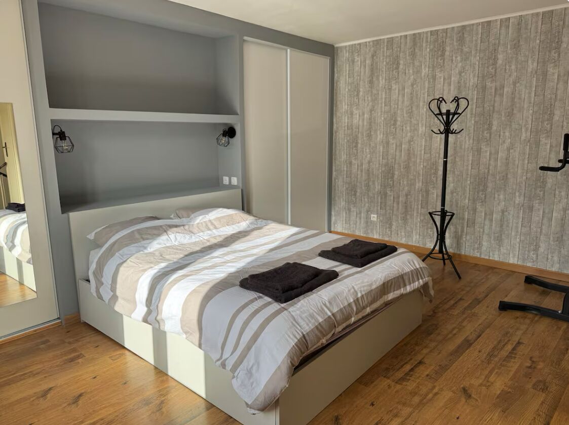 Un dormitorio moderno con una cama, suelo de madera, un armario y una lámpara de pie.