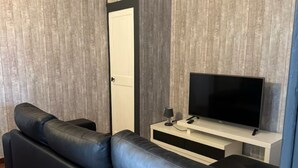 Moderni olohuone, jossa on musta nahkasohva, valkoisella jalustalla oleva taulutelevisio ja puupaneloidut seinät.