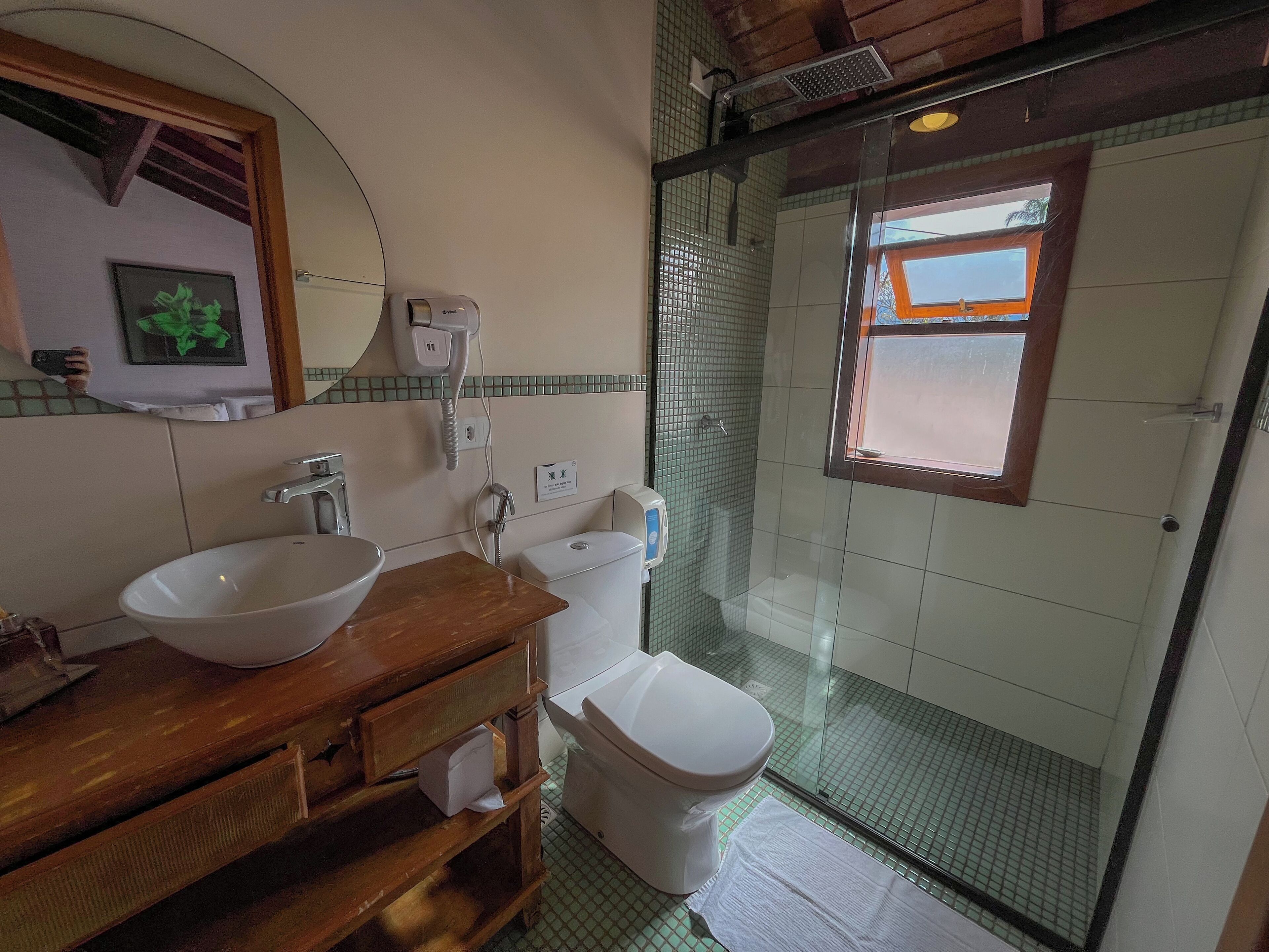 Ein Badezimmer mit einem Holzbadezimmermöbel, einem weißen Waschbecken, einer Toilette und einer gläsernen Duschkabine.