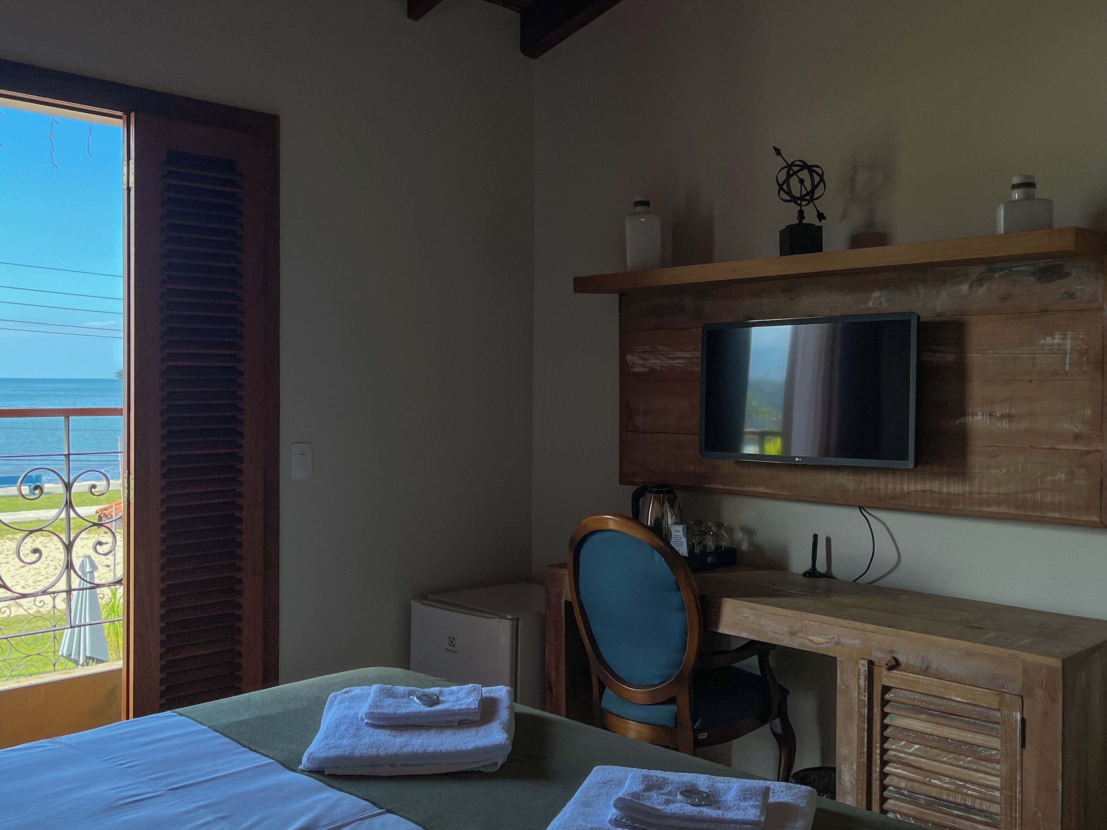 Una habitación con cama, escritorio, silla, televisión y vista al océano.