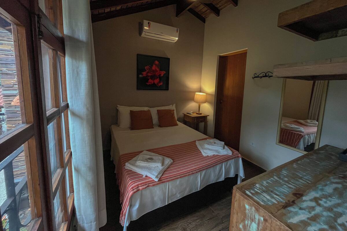 Un dormitorio con cama, mesita de noche, lámpara, aire acondicionado y espejo.