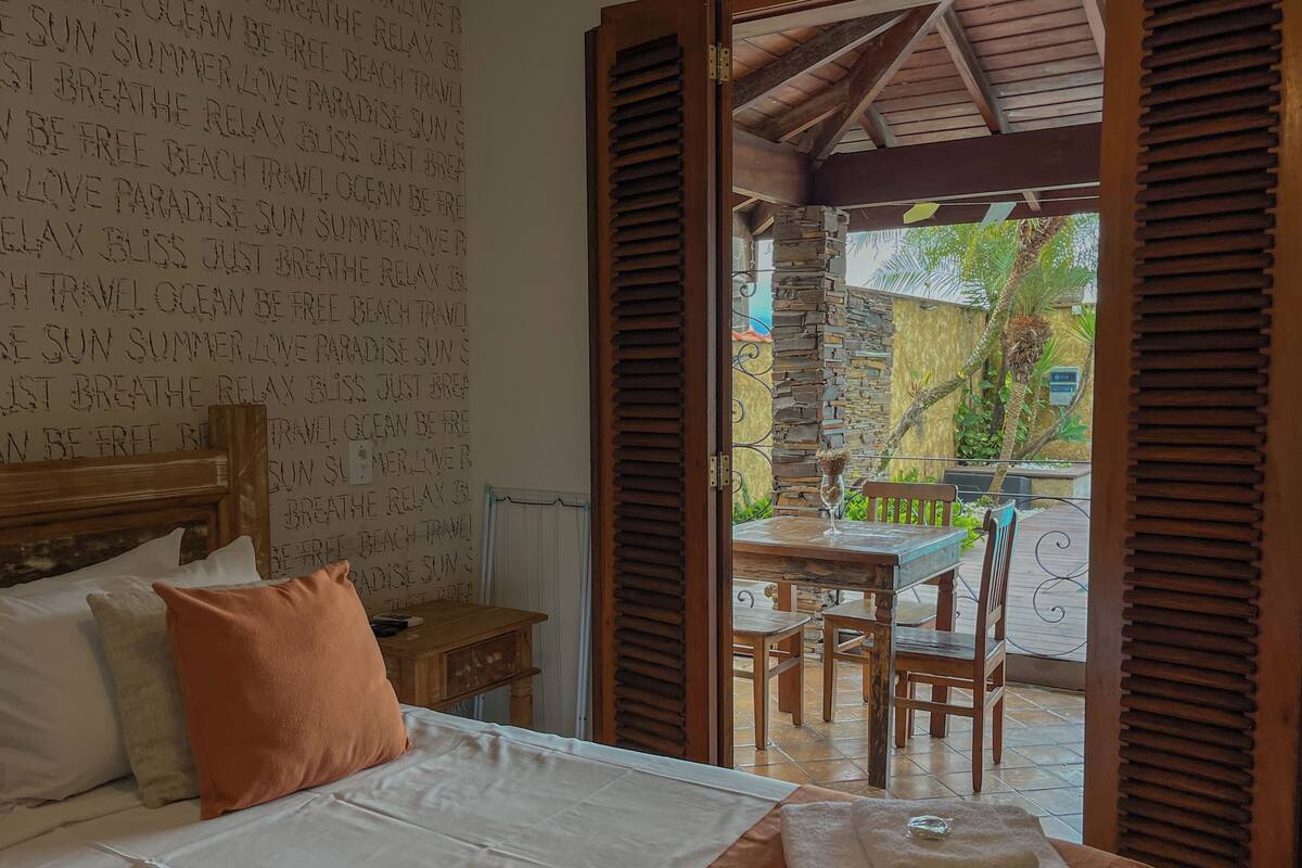 Un dormitorio con cama, almohadas y vistas a un patio exterior con mesa y sillas.