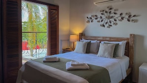 Une chambre d’hôtel équipée d’un lit, d’une table de chevet, d’une lampe, d’un climatiseur et d’un balcon offrant une vue sur les palmiers.