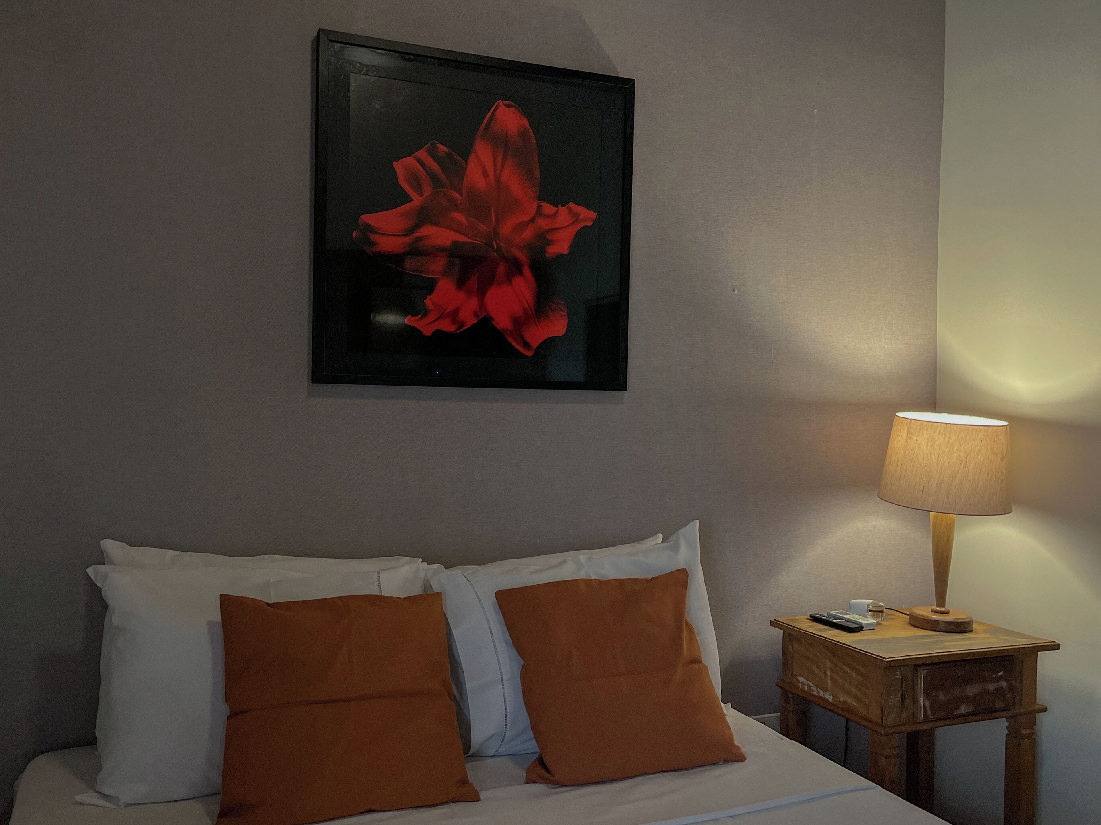 A hotel room with a bed, pillows, a nightstand, a lamp, and a framed artwork on the wall.