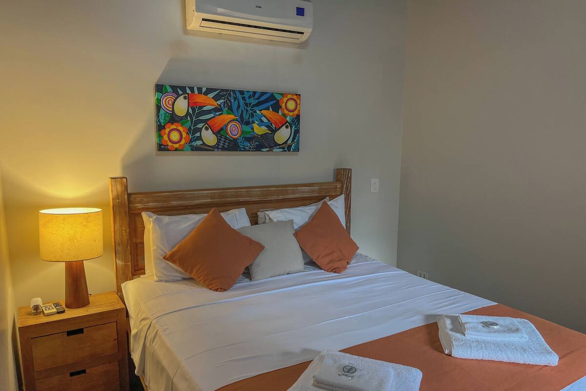 Habitación de hotel con cama, mesita de noche con lámpara, un cuadro en la pared y una toalla sobre la cama.