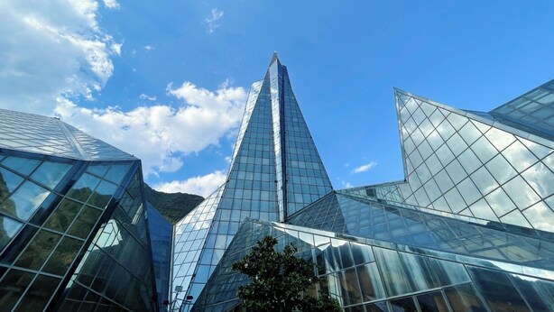 Un bâtiment moderne en verre, de forme triangulaire, entouré d’autres structures également en verre.