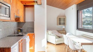 Une cuisine moderne dotée de plans de travail en granit, d’armoires en bois et d’un four encastré. On y trouve un coin repas avec une table et des chaises blanches, ainsi qu’une fenêtre offrant une vue sur un paysage montagneux.