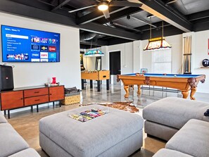 A modern living room with a flat-screen TV, a pool table, and a foosball table.