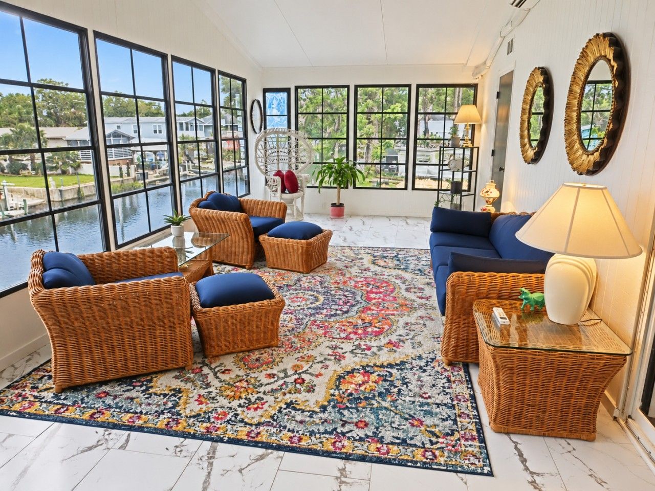 A room with wicker furniture, a blue sofa, and a view of a body of water through large windows.