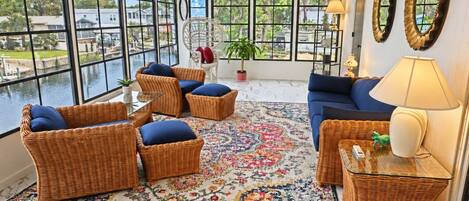 A room with wicker furniture, a blue sofa, and a view of a body of water through large windows.
