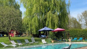 Zwembad met ligbedden en parasols, omringd door groen en bomen.