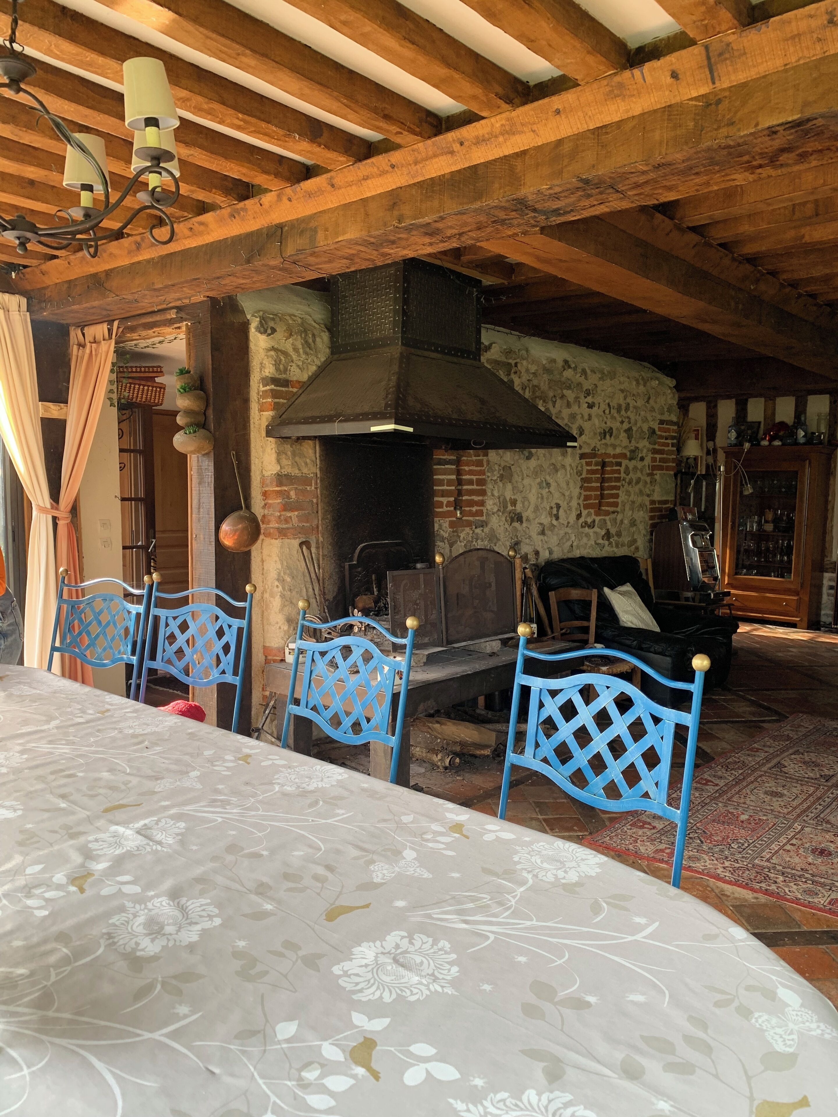 A rustic dining area with a table set for four, blue chairs with a lattice design, a stone wall, and a brick fireplace.