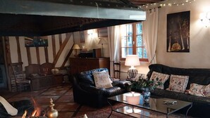 Een gezellige woonkamer met een open haard, een zwarte leren bank, een glazen salontafel en een kamerbreed tapijt met dessin.