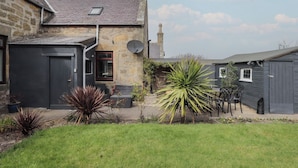 Une maison en pierre avec une porte gris foncé, une petite fenêtre et une antenne parabolique.