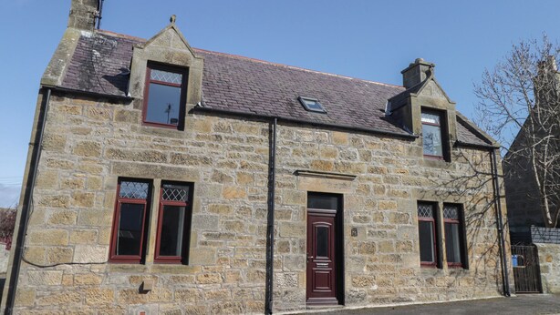 A stone building with a pitched roof, two chimneys, and a door with a window above it. - 6 New Street (Elgin)