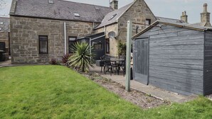 A stone building with a sloped roof, a fenced garden, and a wooden shed. - 6 New Street (Elgin)