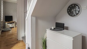 Une pièce avec une commode blanche, une horloge au mur et un téléviseur posé sur un meuble.