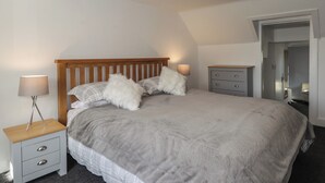A bedroom with a wooden bed, grey bedding, a nightstand with a lamp, and a dresser. - 6 New Street (Elgin)