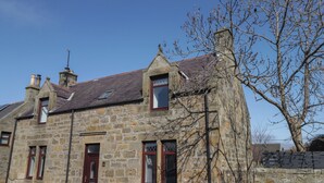 Un bâtiment en pierre avec une porte rouge, de nombreuses fenêtres et une cheminée.