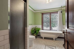 A bathroom with a freestanding bathtub, a toilet, and a window with a view of trees.