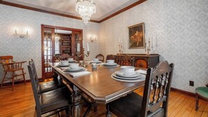 Comedor con mesa de madera dispuesta para seis comensales, sillas a ambos lados, una lámpara de araña y una estantería.