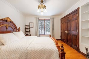 A bedroom with a large bed, a wooden wardrobe, and a chandelier.