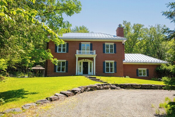 A two-story brick house with a front porch, a stone retaining wall, and a metal roof.