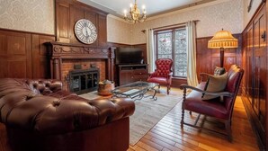 Un salón tradicional con un sofá de cuero, un sillón rojo, una mesa de centro de vidrio, una chimenea y un gran reloj de pared.