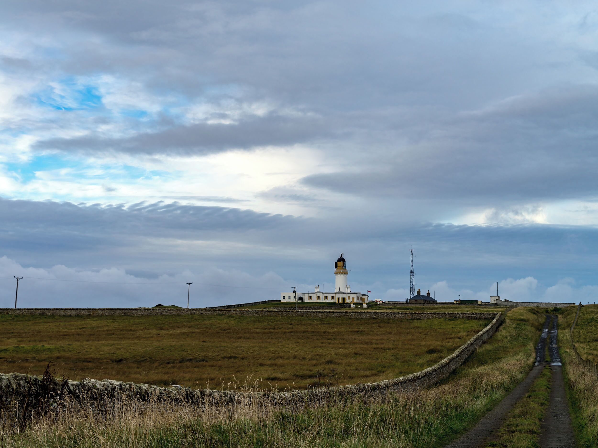 Un phare se dresse sur une colline herbeuse, et un sentier de terre mène jusqu’à lui.