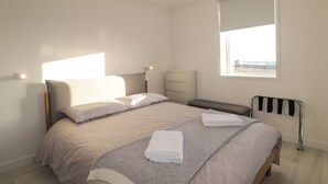 A neatly arranged bedroom with a bed, bedside tables, a window with a view, and a radiator. - The Lighthouse Keepers Cabin (Wick)