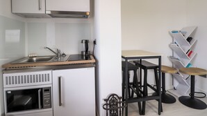 A compact kitchen with white cabinets, a built-in microwave, a coffee maker, and a small sink. There are two stools and a metal rack against the wall. - The Lighthouse Keepers Cabin (Wick)
