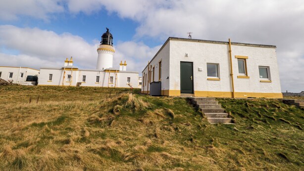 A lighthouse with a white building next to it, both featuring a simple, functional design. - The Lighthouse Keepers Cabin (Wick)