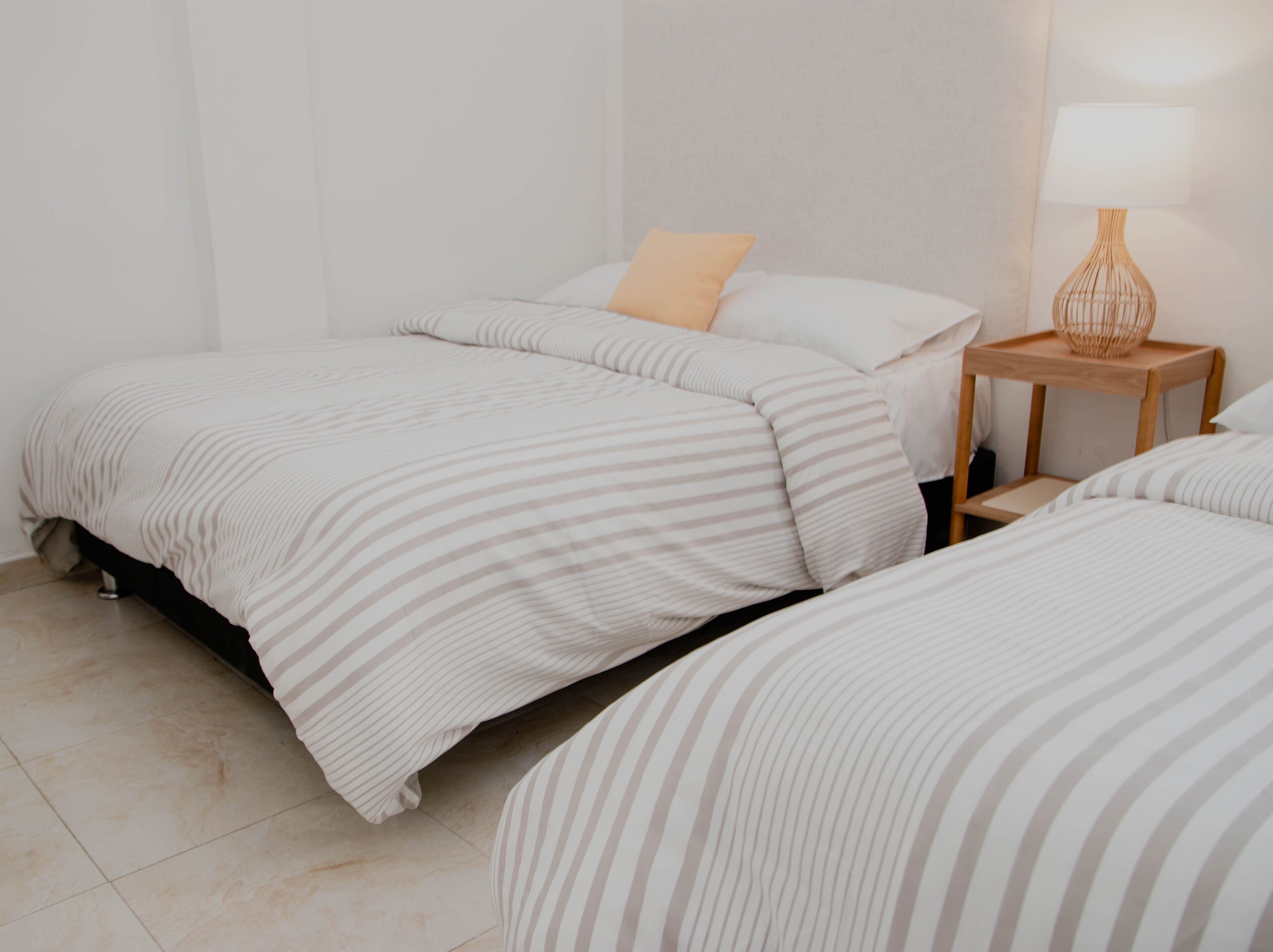 Ein Schlafzimmer mit zwei Betten, einem Nachttisch mit Lampe und einer schlichten Wand.