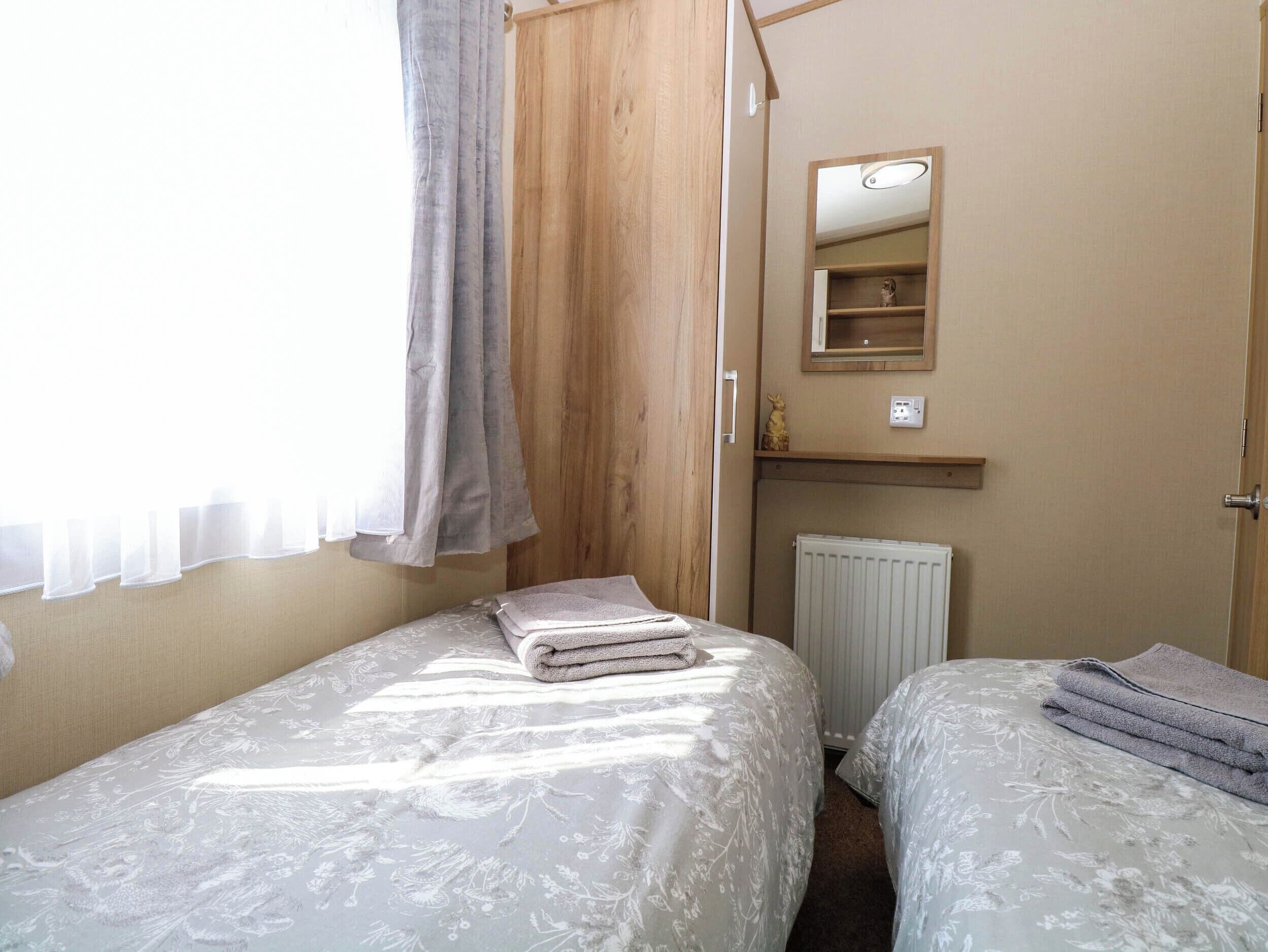 A bedroom with two beds, a wooden wardrobe, a radiator, and a mirror on the wall.