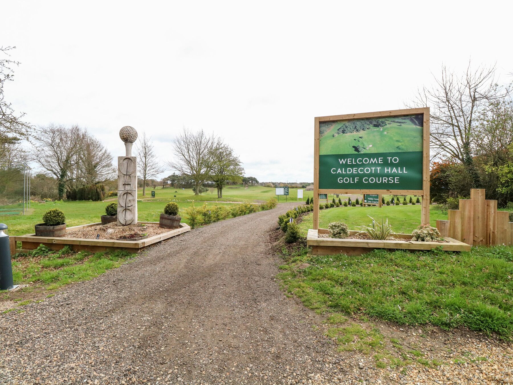 A gravel path leading to a golf course entrance with a welcome sign.