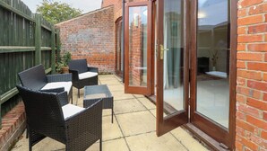 A patio with wicker furniture and a glass door leading to a room. - Willow (Dereham)