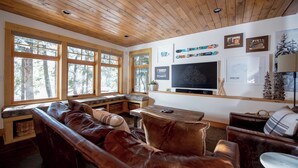Una sala de estar acogedora con un sofá de cuero, techo de madera, ventanas amplias, un televisor de pantalla plana y diversas decoraciones en las paredes.