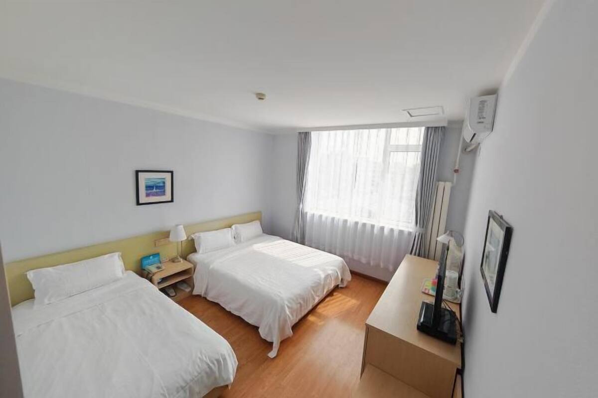 A hotel room with two beds, a desk, a chair, a window with curtains, and a picture on the wall.