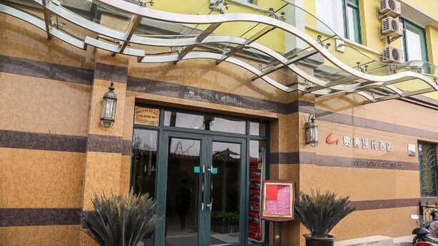 Entrada de hotel con puerta de vidrio, plantas en macetas y un cartel.